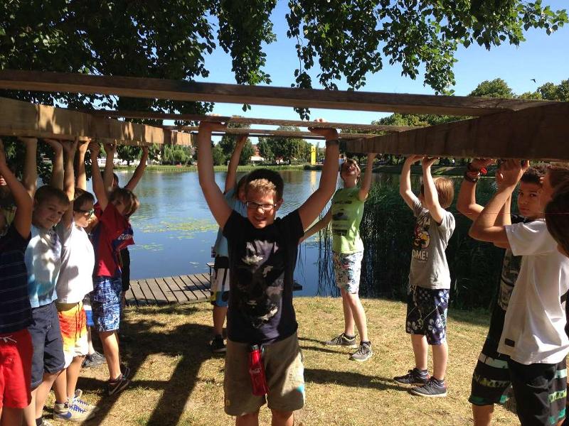 Kinder tragen im Outdoorcamp Holzbalken über dem Kopf