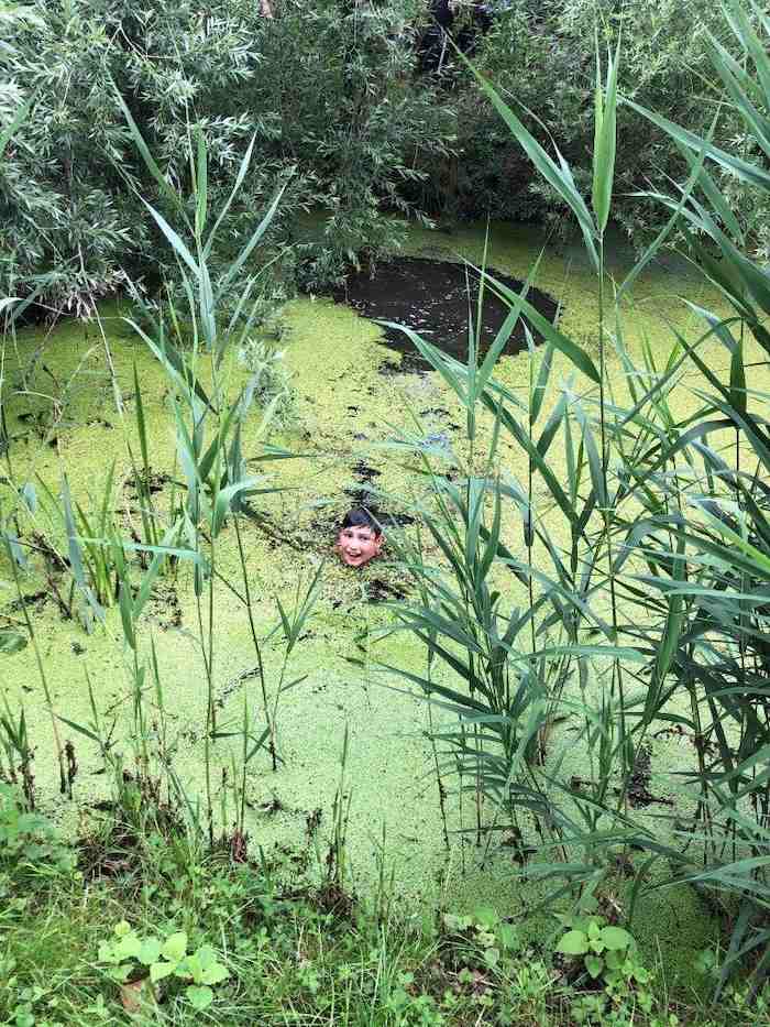 Im Abenteuercamp geht ein Junge in einem Tümpel baden
