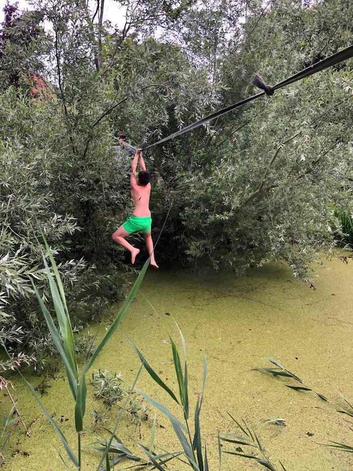 Kinder hangeln sich während der Ferienbetreuung mit einem Seil über einen Tümpel