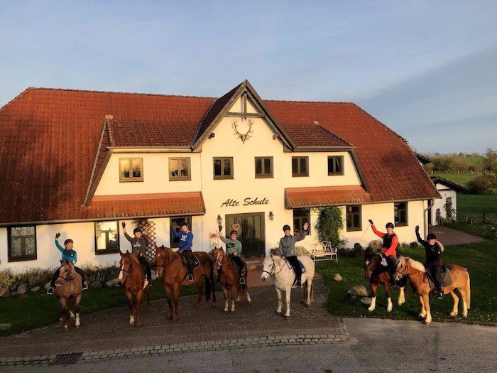 Kinder sitzen auf den Ferien auf dem Ponyhof auf den Pferden und winken
