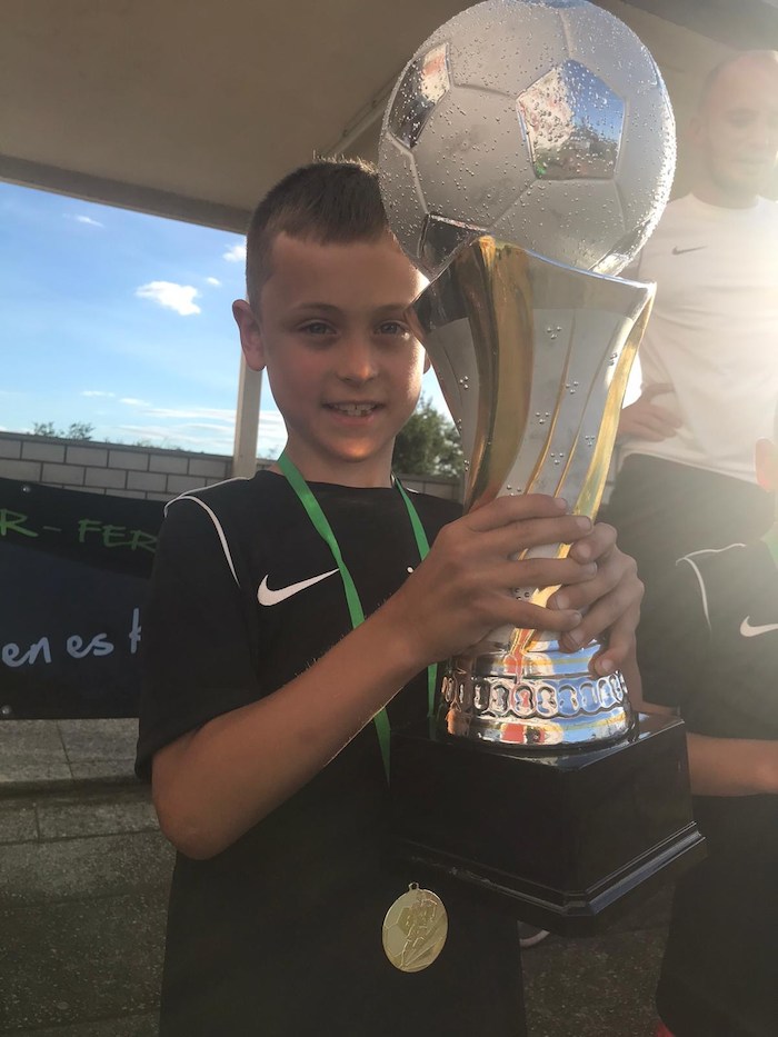Ein Junge hält im Fußballcamp Deutschland einen Pokal hoch