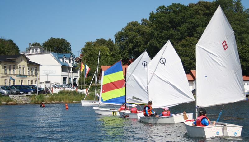 Die Kinder aus dem Segelcamp sitzen beim Segeln auf dem Wasser in ihren Booten.