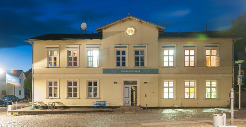 Die Unterkunft im Windsurfcamp prahlt mit einer weißen Fassade und vielen Lichtern, das aus den Fenster strahlt.