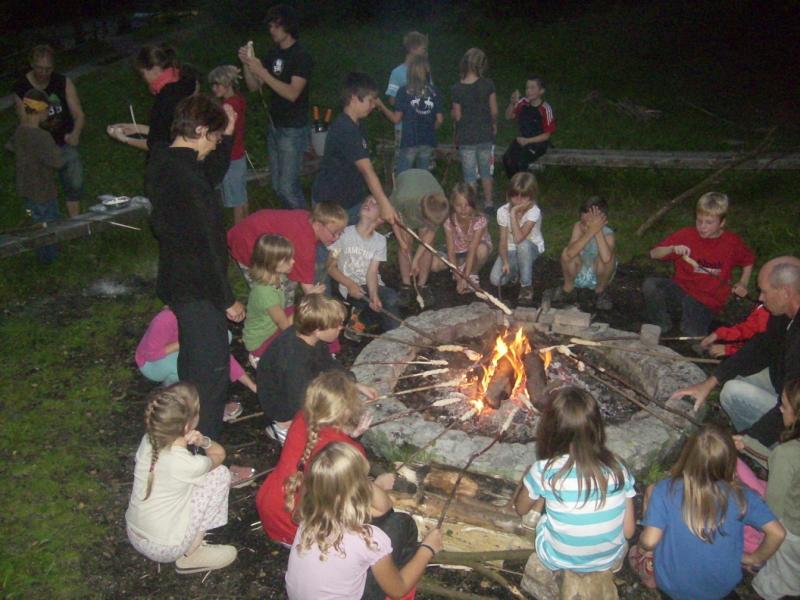 Eine Gruppe Kinder braten sich gemeinsam über dem Lagerfeuer Stockbrot