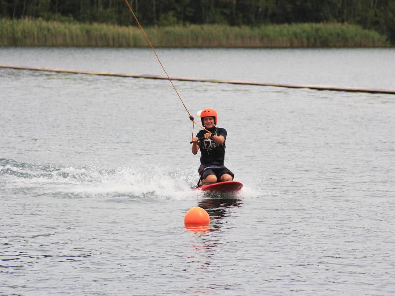 Ein Junge eines Wakeboard Camps fährt auf den Knien Wakeboard
