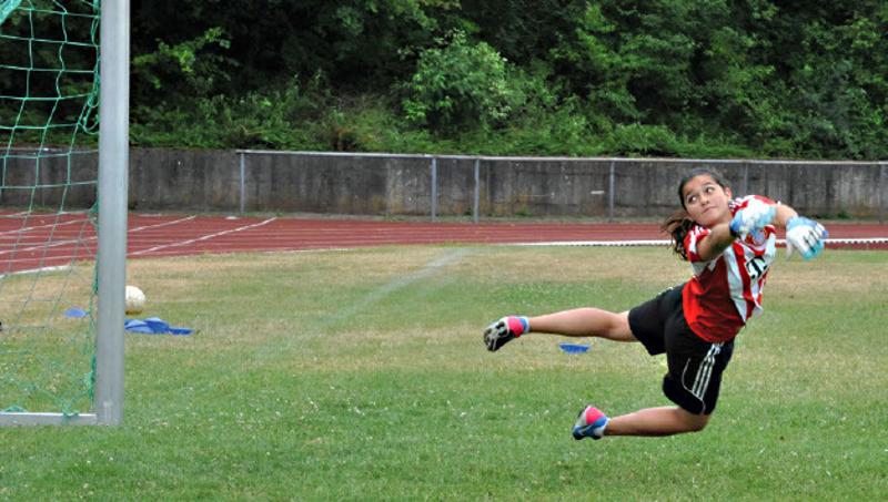 Eine Torwärtin springt im Fußballcamp, um den Ball zu kriegen