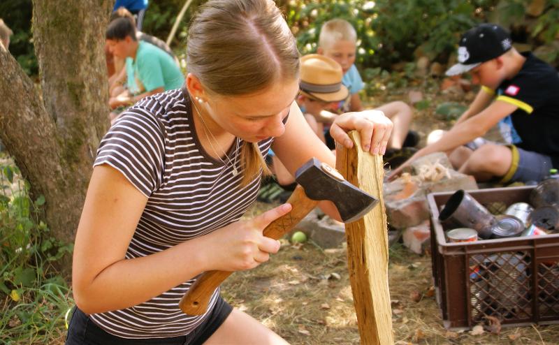 Ein Mädchen bearbeitet Holz im Abenteuer Ferienlager mit der Axt.