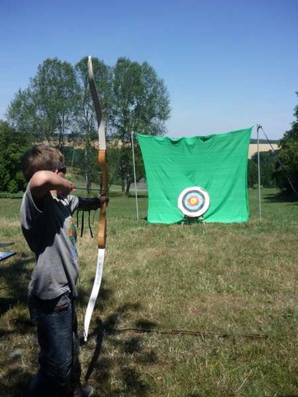 Ein Junge spannt im Abenteuer Ferienlager den Bogen, um die Zielscheibe zu treffen.