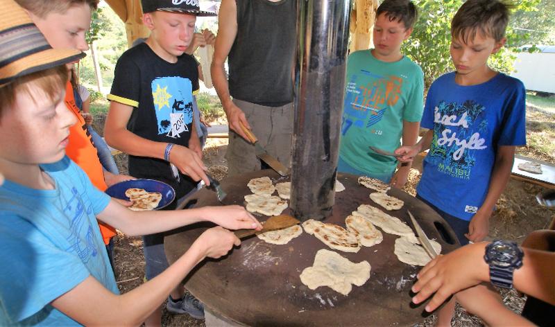 Die Kinder stehen im Kreis und bereiten im Abenteuer Ferienlager Brot zu.