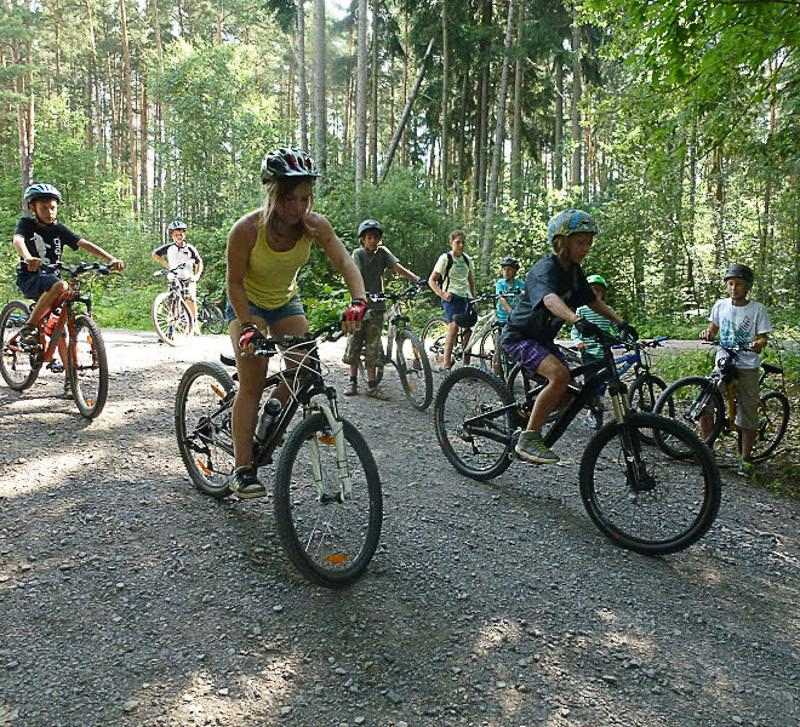 Die Kinder machen im Abenteuercamp eine Fahrradtour durch den Wald.