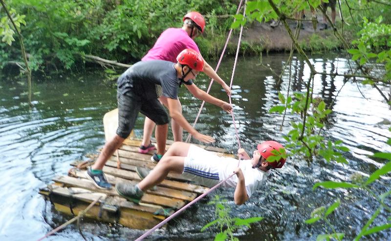 Mit Seilen als Absicherung probieren die Kids im Abenteuercamp ihr Floß auf dem Wasser aus.