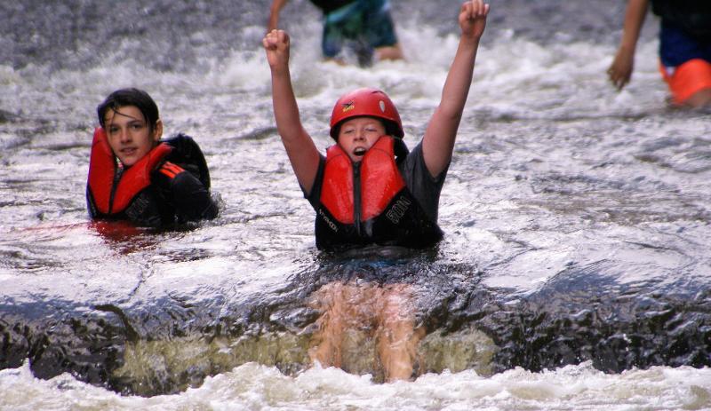 Kinder baden im Abenteuer Ferienlager im Fluss mit einer Weste.