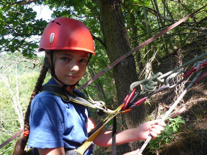 Ein Mädchen aus dem Abenteuer-Camp ist beim Kletter von vielen Seilen gesichert.