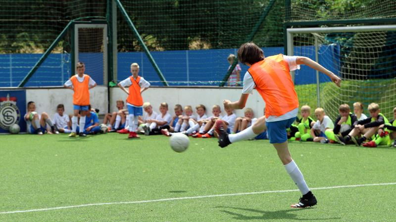 Ein Junge einer Fußball-Schule Ferien schießt einen hohen Ball