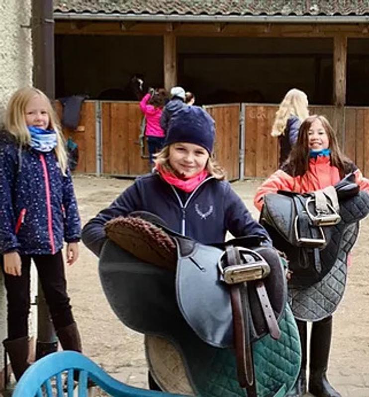 Kinder der Reiterferien für Kinder tragen Sättel
