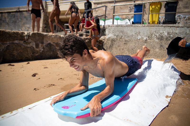 Ein Junge rutscht im Portugal Surfcamp mit dem Board über eine Rutsche am Strand