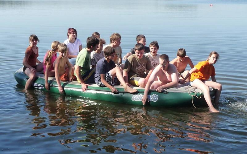 Während der Ferienbetreuung Sommerferien fahren viele Kinder mit einem Schlauchboot über einen See