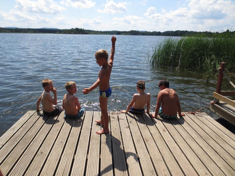 Die Kinder sitzen während der Ferienbetreuung auf einem Steg am See