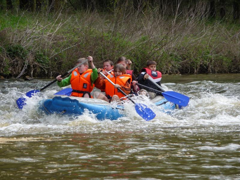 Kinder paddeln mit einem Boot während der Ferienbetreuung Sommerferien durch einen Fluss
