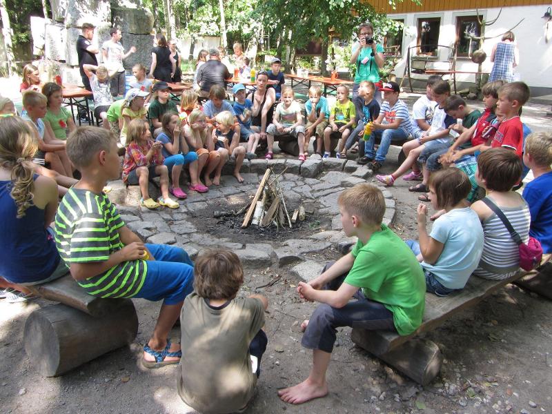Bei der Ferienbetreuung Sommerferien sitzen die Kinder am Lagerfeuerplatz