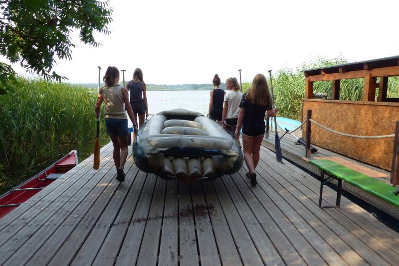 Ein paar Kinder tragen während der Ferienbetreuung Sommerferien ein Schlauchboot zum Wasser