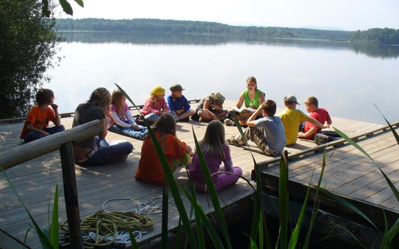 Eine Betreuerin liest den Kindern während der Ferienbetreuung am Steg etwas vor