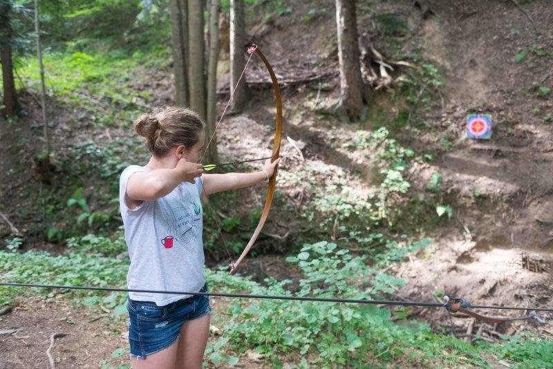 Ein Mädchen eines Abenteuer Forschercamps schießt mit Pfeil und Bogen