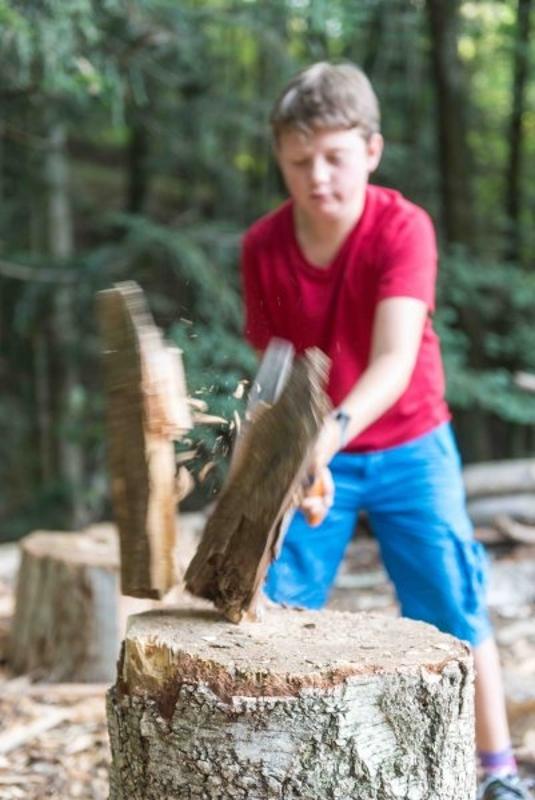 Ein Junge eines Abenteuer Forschercamps fällt Holz