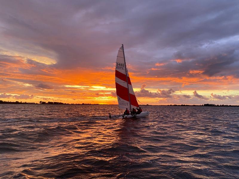Teilnehmer eines Feriencamps am Wasser segeln im Sonnenuntergang
