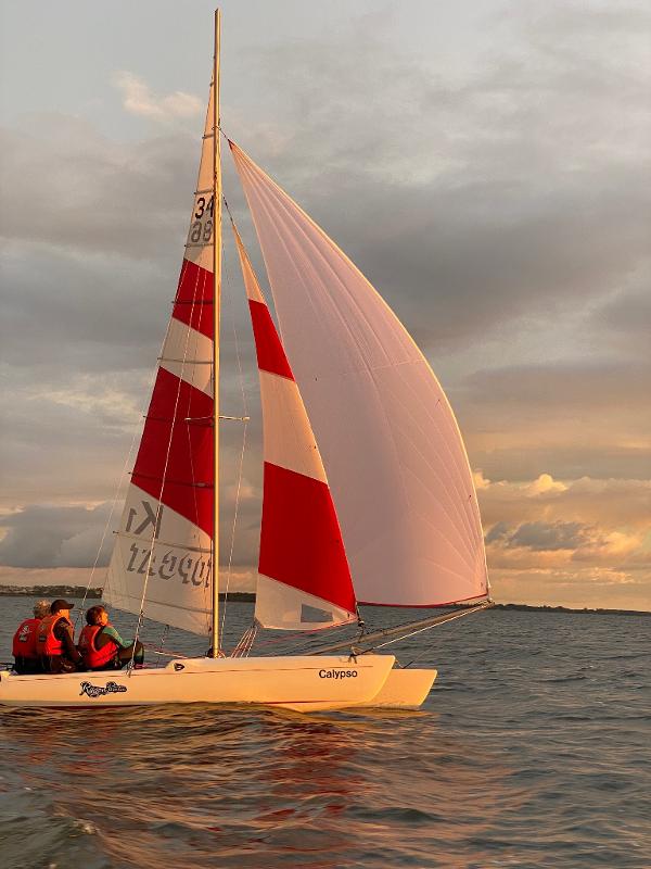 In der Abendröte segeln Teilnehmer eines Feriencamps am Wasser