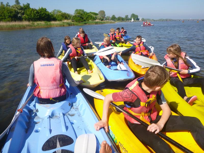 Kinder eines Feriencamps am Wasser fahren Kajak
