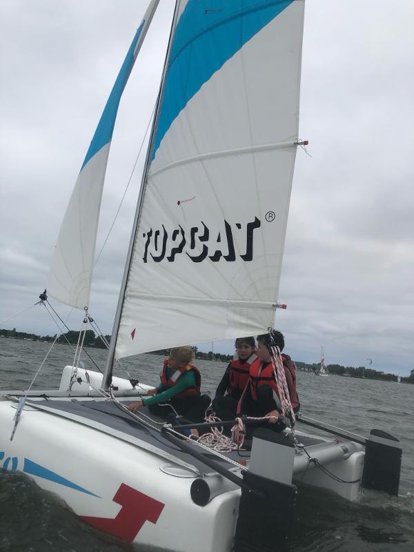 Jungs eines Feriencamps am Wasser hissen das Segel