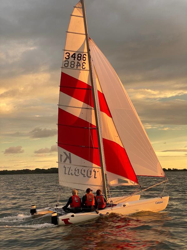 Im Abendlicht segeln Teilnehmer eines Feriencamps am Wasser