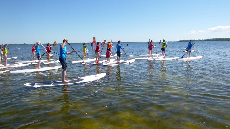Kinder eines Feriencamps am Wasser fahren SUB