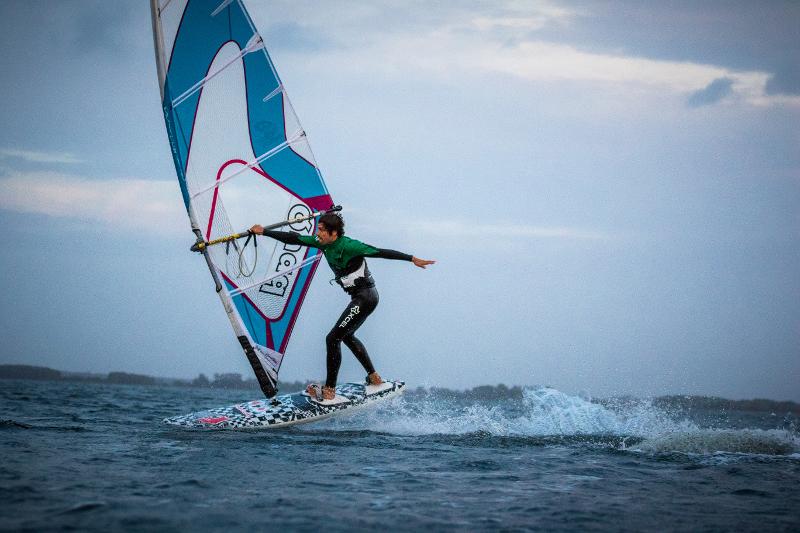 Ein Junge macht im Windsurfcamp einen coolen Stunt mit nur einer Hand am Segel.