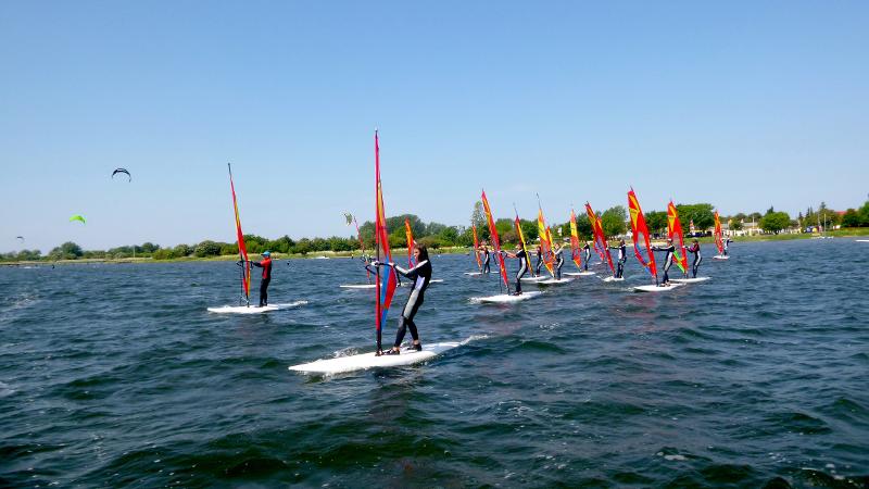Die Teilnehmer gleiten auf den Boards im Windsurfcamp über das Wasser.