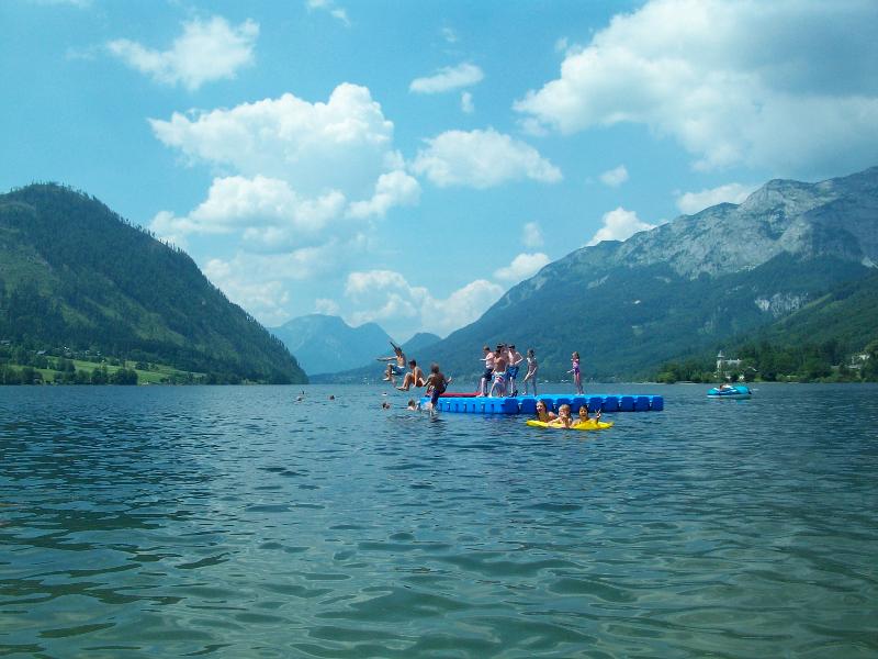 Die Kinder haben Spaß auf einer Schwimminsel und springen im Outdoorcamp in den See