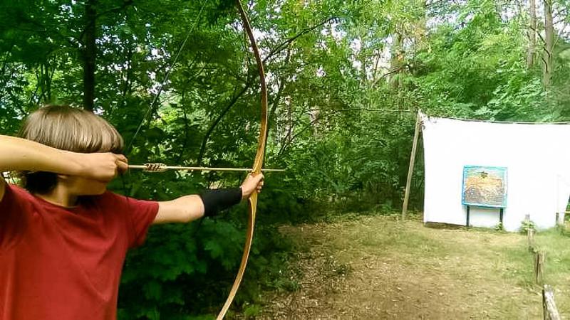Teilnehmer eines Zeltcamps schießen mit Pfeil und Bogen