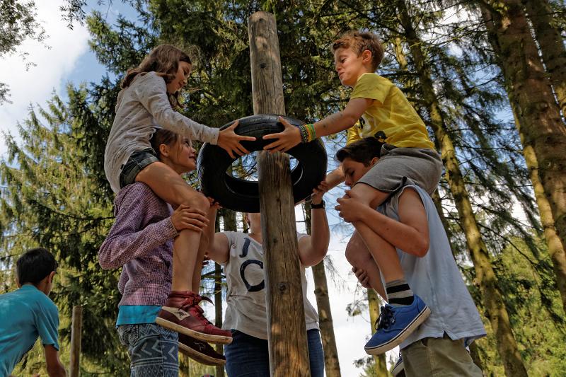 Die Kinder heben gemeinsam im Sportcamp einen Reifen von einem Baumstamm