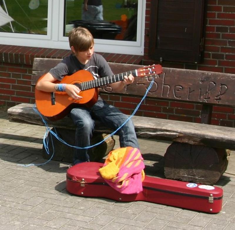 Ein Junge spielt bei einem Feriencamp Hannover vor einem Haus Gitarre