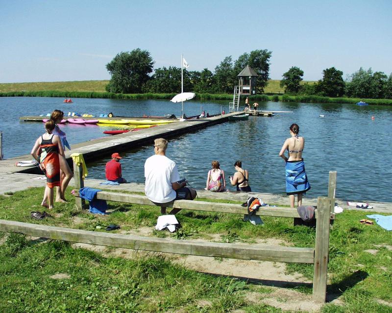 Teilnehmer sitzen im Feriencamp Hannover an einem See auf einem Steg