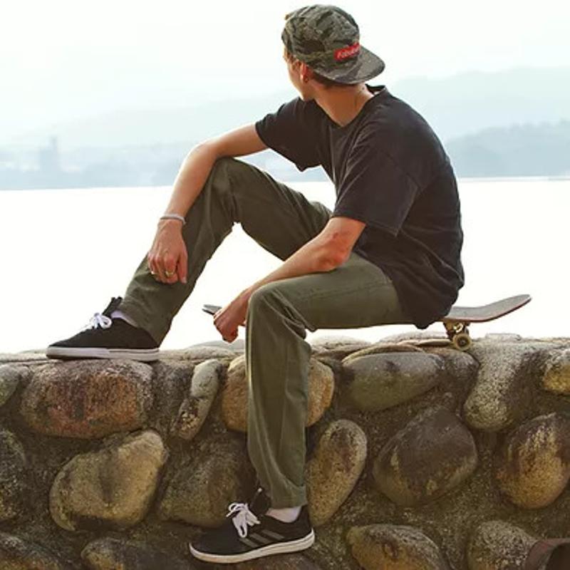 Ein Teilnehmer der Jugendreise Calella sitzt mit seinem Skateboard auf einer Mauer