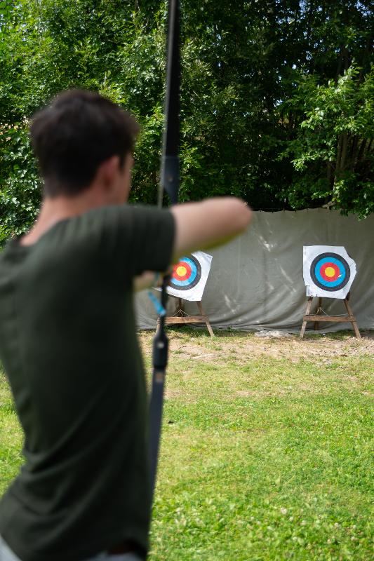 Ein Junge zielt mit Pfeil und Bogen während der Ferienbetreuung auf eine Zielscheibe