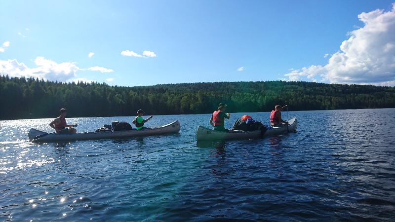 Bei der Ferienbetreuung fahren die Teilnehmer mit mehreren Kanus im Sonnenschein über den See