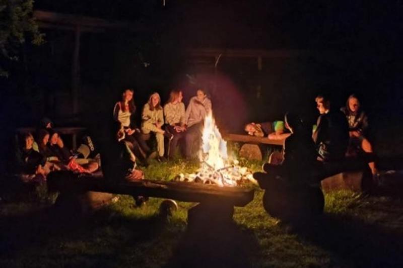 Eine Gruppe Kinder Kinder und Jugendliche sitzt am Lagerfeuer im Ferienlager Deetz.