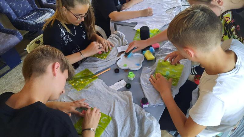 In den Winterferien Leipzig basteln Kinder an einem Tisch an T-Shirts