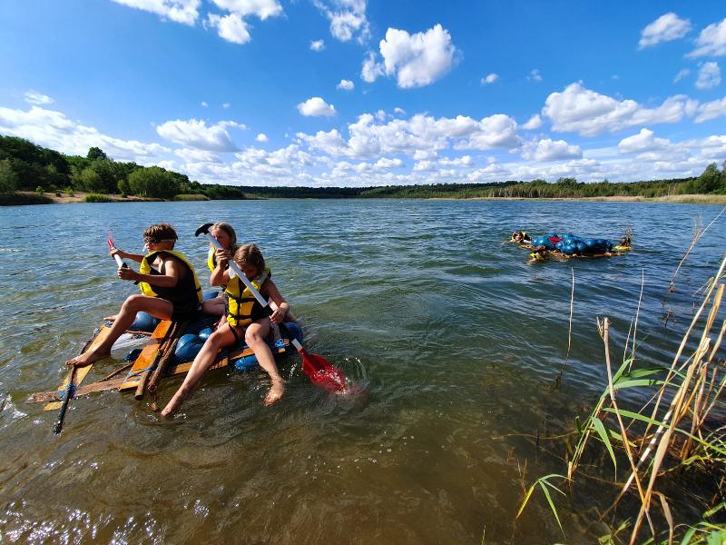 Kinder fahren im Outdoorcamp mit einem Floß auf einem See