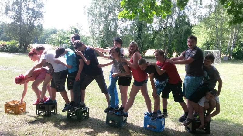 Die Kinder balancieren auf wenigen Kisten im Outdoorcamp einen Weg entlang