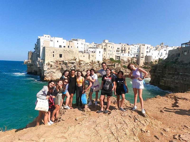 Eine Gruppe Jugendlicher steht während der Sprachreise Italien Schüler vor einer Burg am Wasser