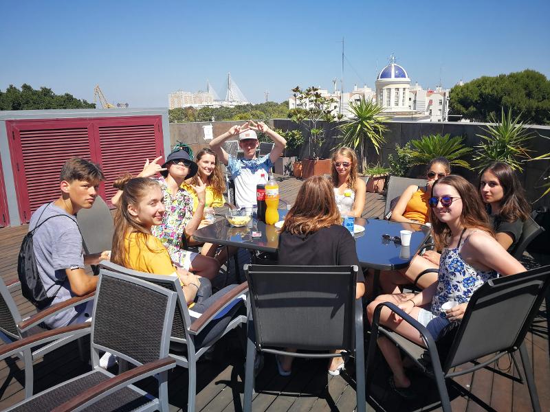 Mehrere Jugendliche sitzen zusammen im draußen auf einer sehr großen Terrasse und genießen die Zeit in der Sonne zusammen bei den Sprachreisen Spanien für Schüler Sommerferien
